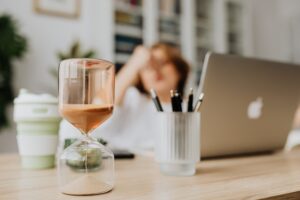 Photo d'une femme devant son ordinateur avec un sablier en premier plan